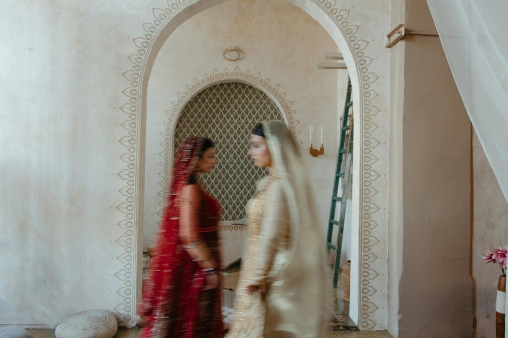 Two women in traditional Indian dress moving gracefully in front of an ornate archway, captured in motion blur.